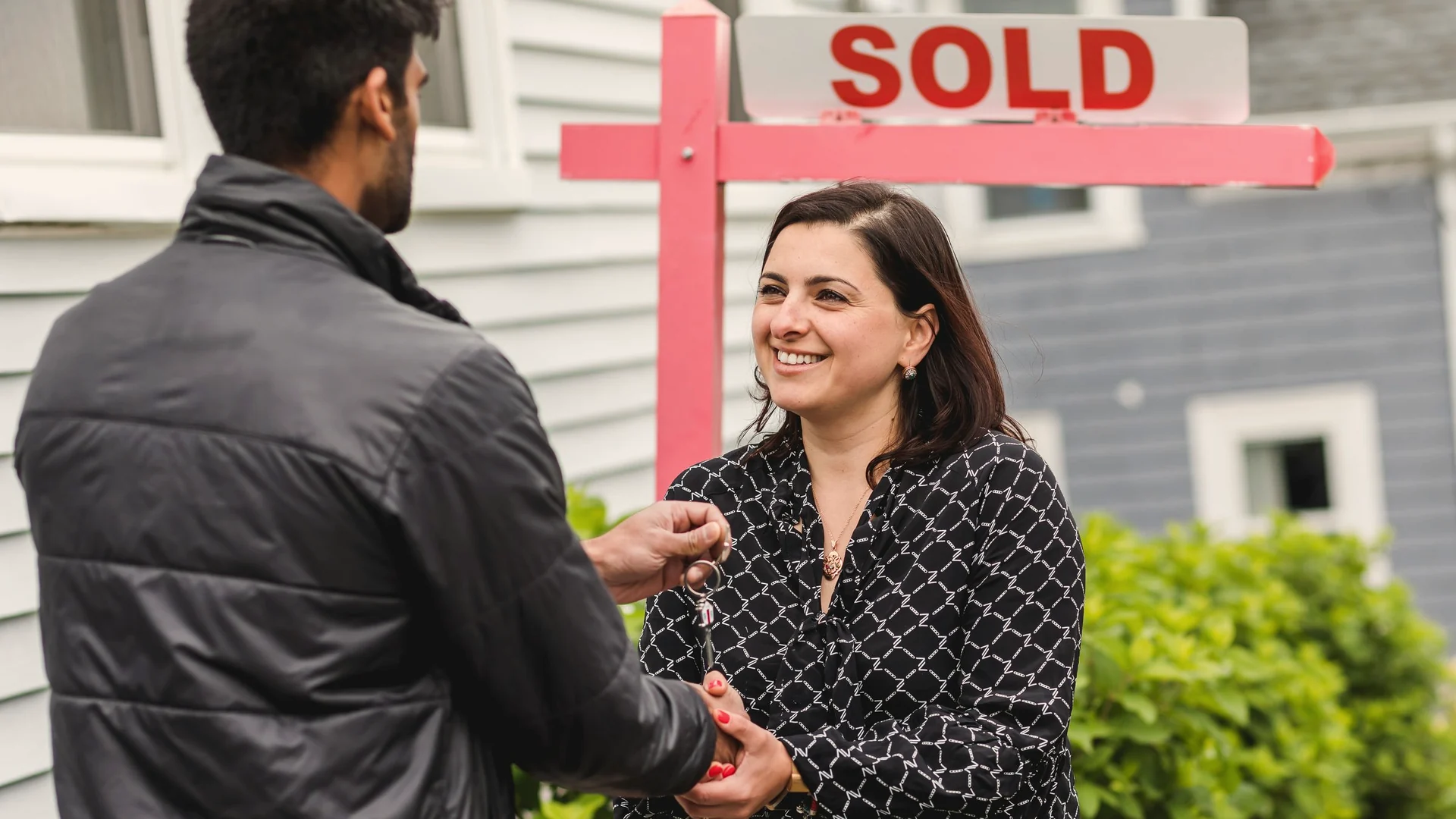 Homebuyer receiving keys in front of a sold house